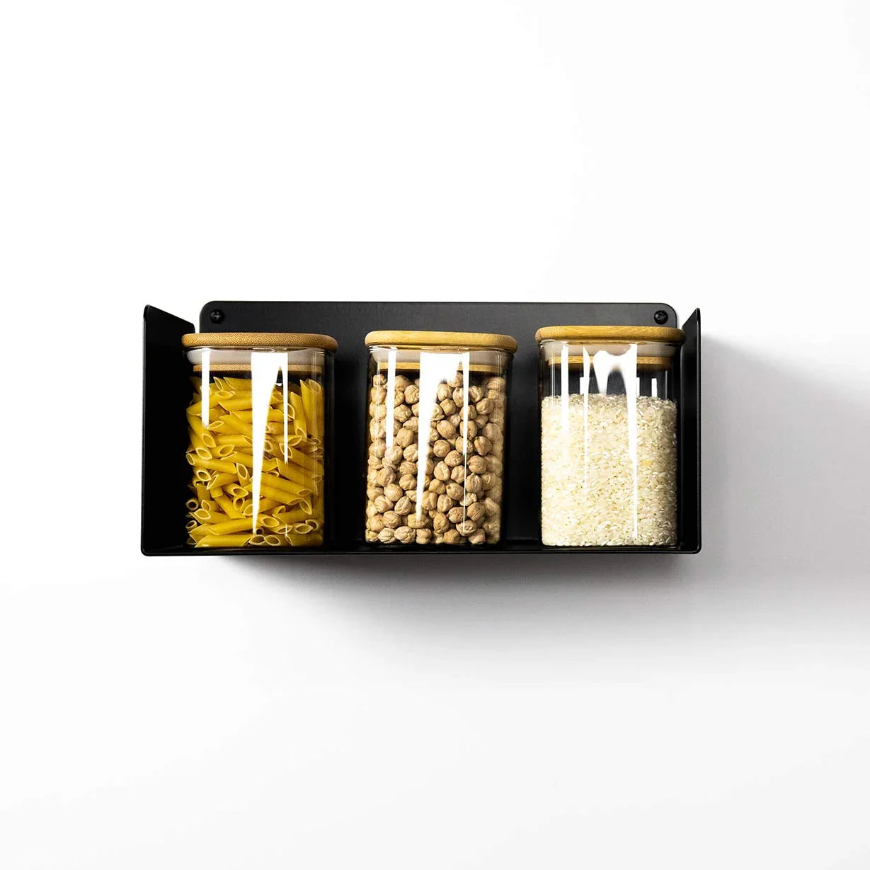 Estante flotante negro minimalista con tarros de vidrio para cocina, almacenando pasta, garbanzos y arroz.