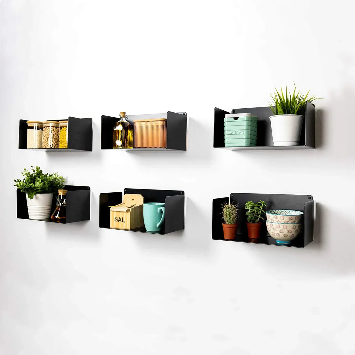 Estantes flotantes de metal negro en pared, decorados con plantas, tazas y utensilios de cocina