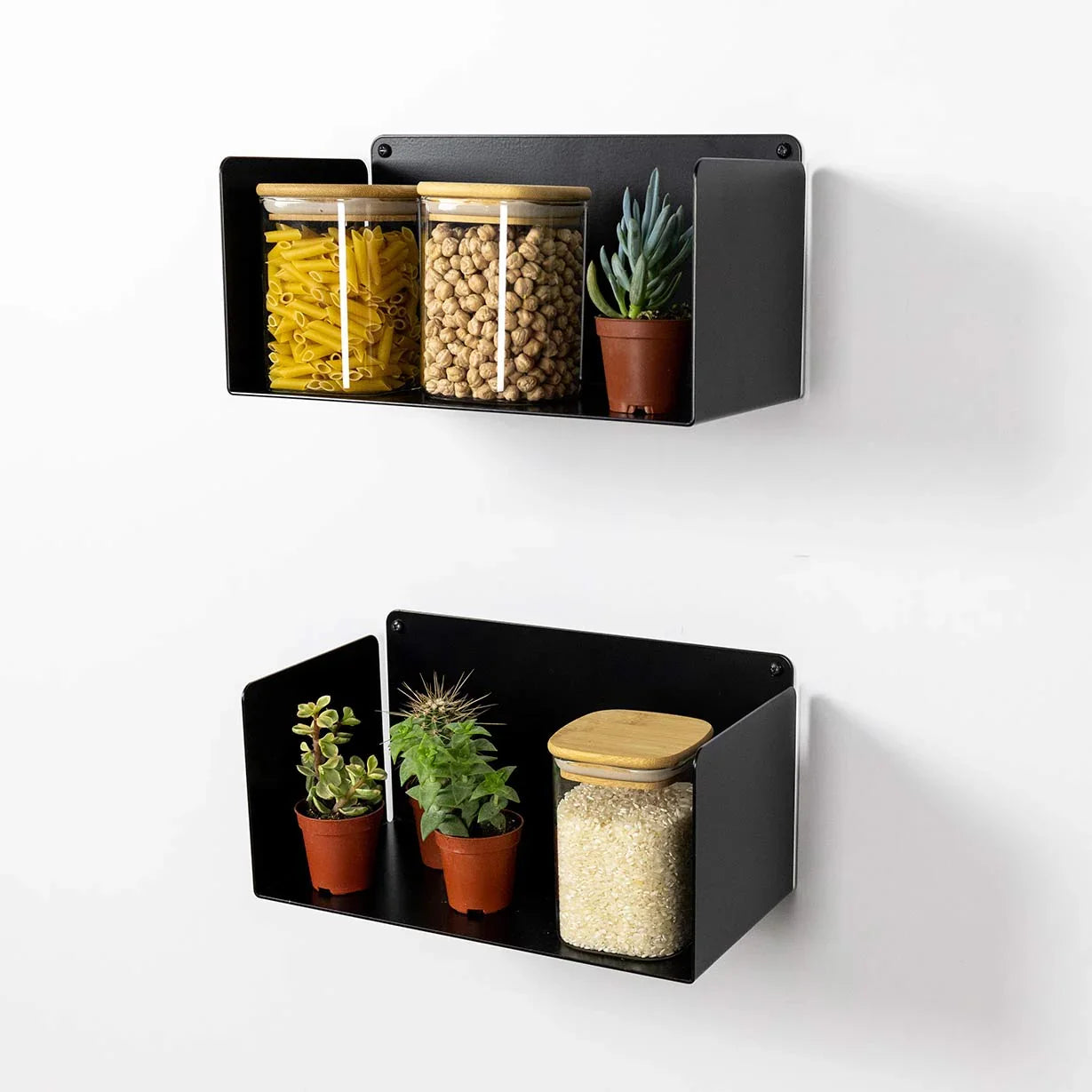 Estantes flotantes de metal negro en pared de cocina con tarros y pequeñas plantas decorativas.