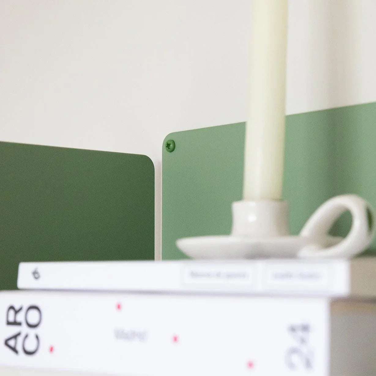 Estante verde de metal colgado en la pared con libros y vela, estilo dopamine decor y moderno