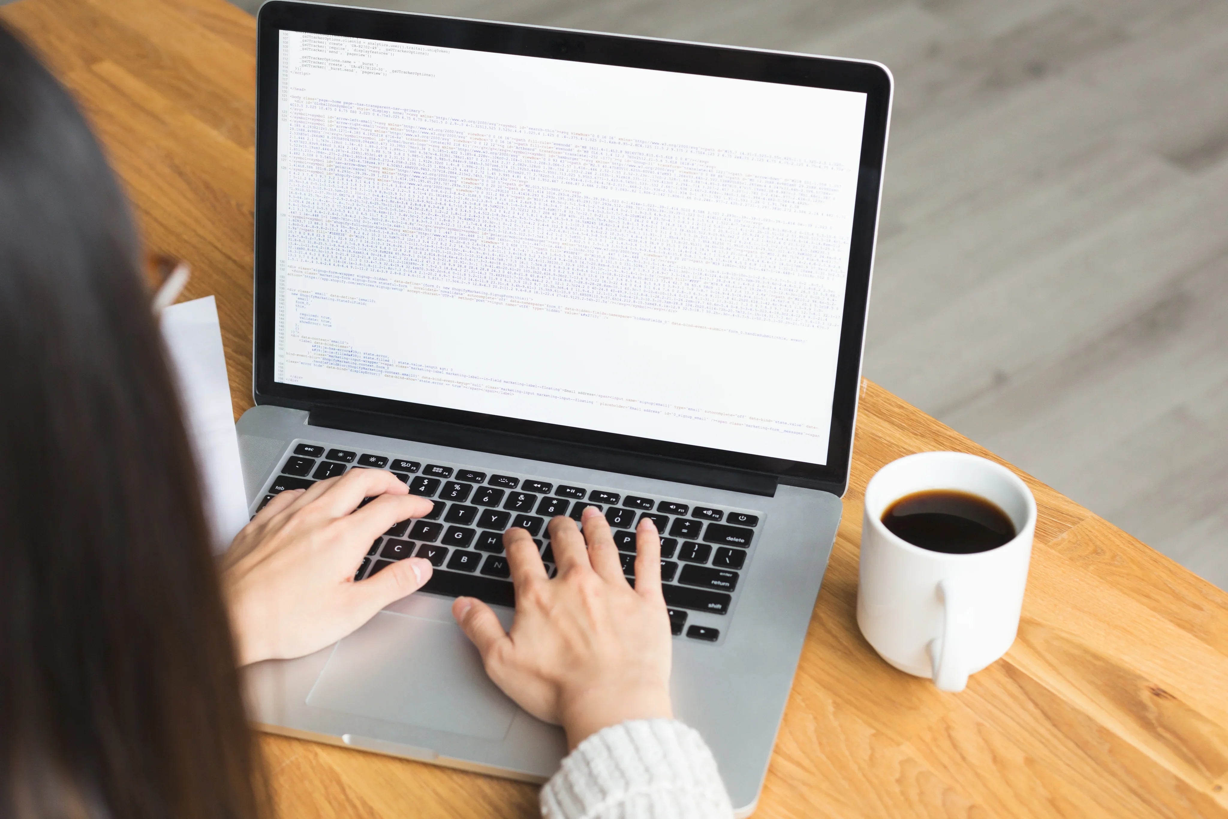Persona programando en portátil sobre mesa de madera junto a una taza de café