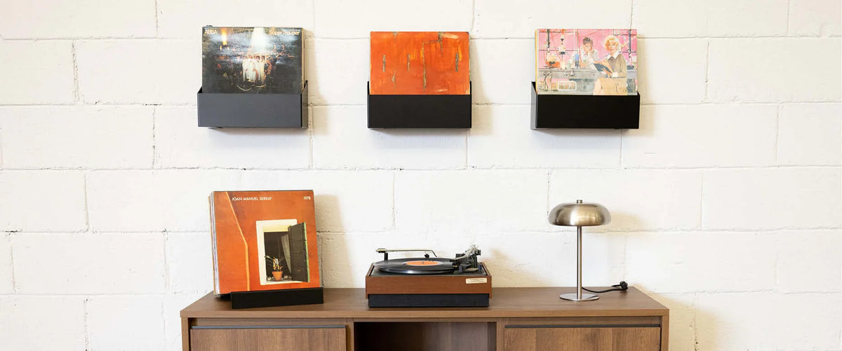 Estantes flotantes negros con vinilos decorativos, tocadiscos y lámpara sobre mueble minimalista