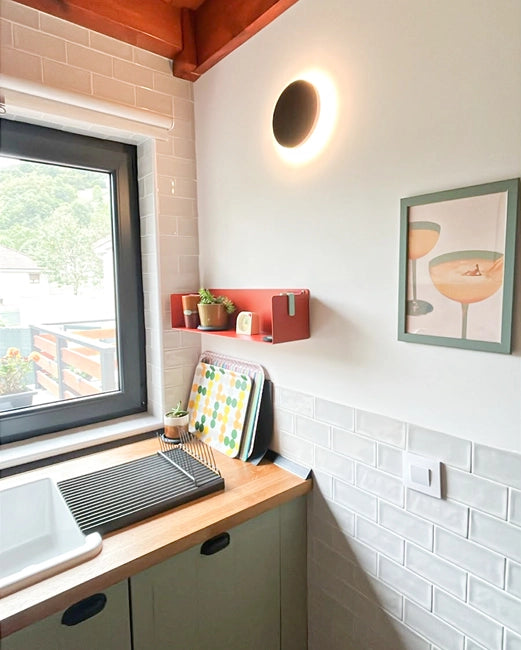 Terracotta-colored metal floating shelf on a kitchen wall with utensils and jars