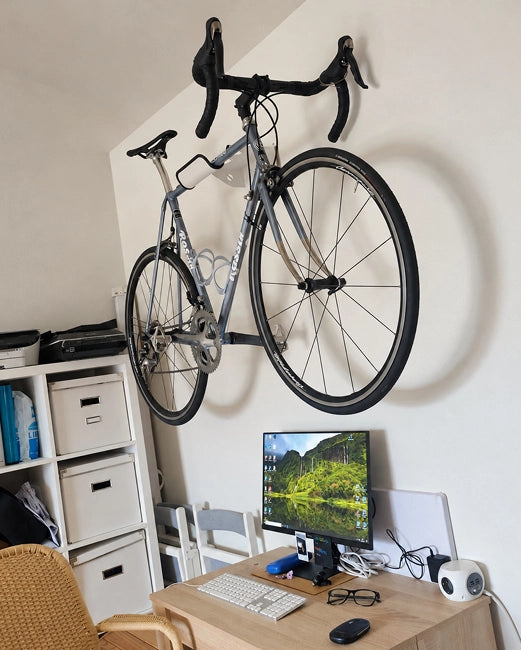 bicicleta colgada en soporte metálico blanco en pared encima de mesa